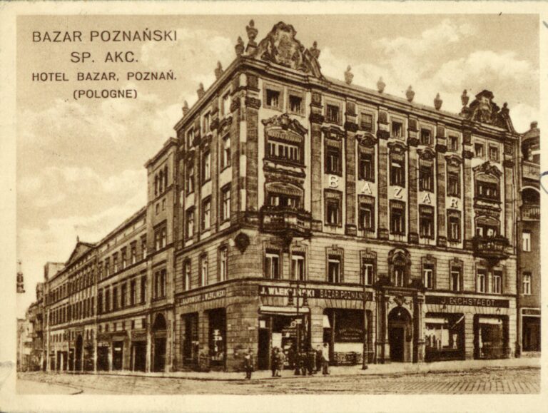 Bazar Poznański w Poznaniu w 1911 roku- widokówka przedstawiająca hotel i restaurację narożny budynek przy brukowanej ulicy, cztery kondygnacje prostokątne okna okrągłe balkony, na parterze sklepy punkty usługowe, na jednym szyld J Wlekliński bazar poznański