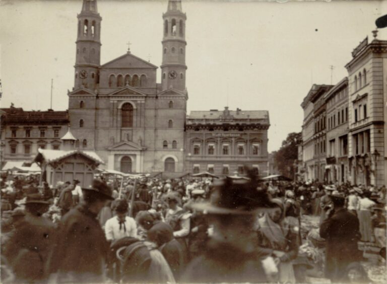 Handel na Starym Rynku w Bydgoszczy, początek XX wieku tłum ludzi na płycie rynku w tle budynek kościoła z dwiema strzelistymi wieżami przylegają do niego z każdej strony dwa trzykondygnacyjne budynki