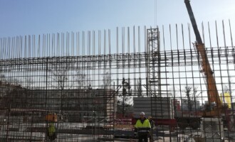 Wykonanie północnej ściany parteru budynku. Instalowanie dźwigu Wykonanie północnej ściany parteru budynku. Instalowanie dźwigu, widoczne zbrojenie stalowe ściany parteru od strony północnej, robotnicy w kaskach i ubraniach ochronnych