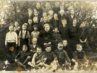 Uczniowie szkoły w Murowańcu- przełom lat 40/50- tych XX wieku, uśmiechnięta grupa dzieci w kilku rzędach w środku nauczycielka, stoją na tle rozłożystego drzewa