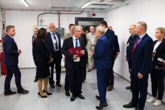 Goście zwiedzają pomieszczenie serwerowni, kilkanaście osób między innymi minister